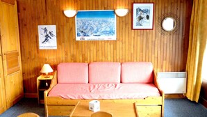 Une pièce chaleureuse avec un mur en bois, un canapé rose, une petite table avec des chaises et un lit.