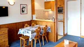 Une cuisine compacte avec des meubles en bois, un four à micro-ondes et un évier. On y trouve une table à manger avec des chaises et un téléviseur fixé au mur.