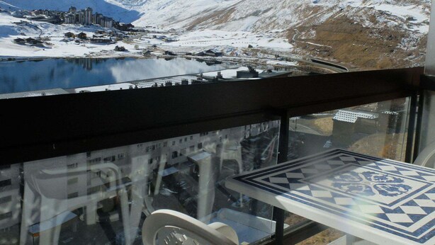 Une vue sur la montagne, avec un lac, des bâtiments et une table recouverte d’une nappe à motifs.