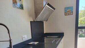 A kitchen with a black countertop, stainless steel sink, and a vent hood. There are two wall-mounted posters, one of which reads "BANANIA" and the other "Hamburgers".