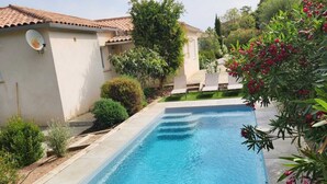 Ein rechteckiger Pool mit zwei Liegestühlen an einer Seite und einem kleinen Gartenbereich mit Baum und Sträuchern.