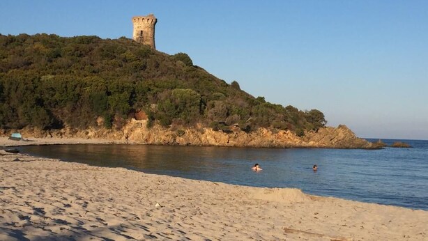 Ein Strand mit einer Burg auf einem Hügel, bewölkter Himmel und ruhigem Meer.