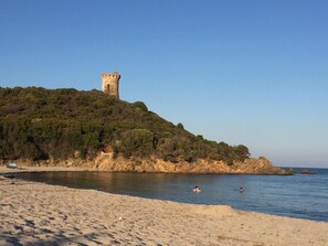 Ein Strand mit einer Burg auf einem Hügel, bewölkter Himmel und ruhigem Meer.