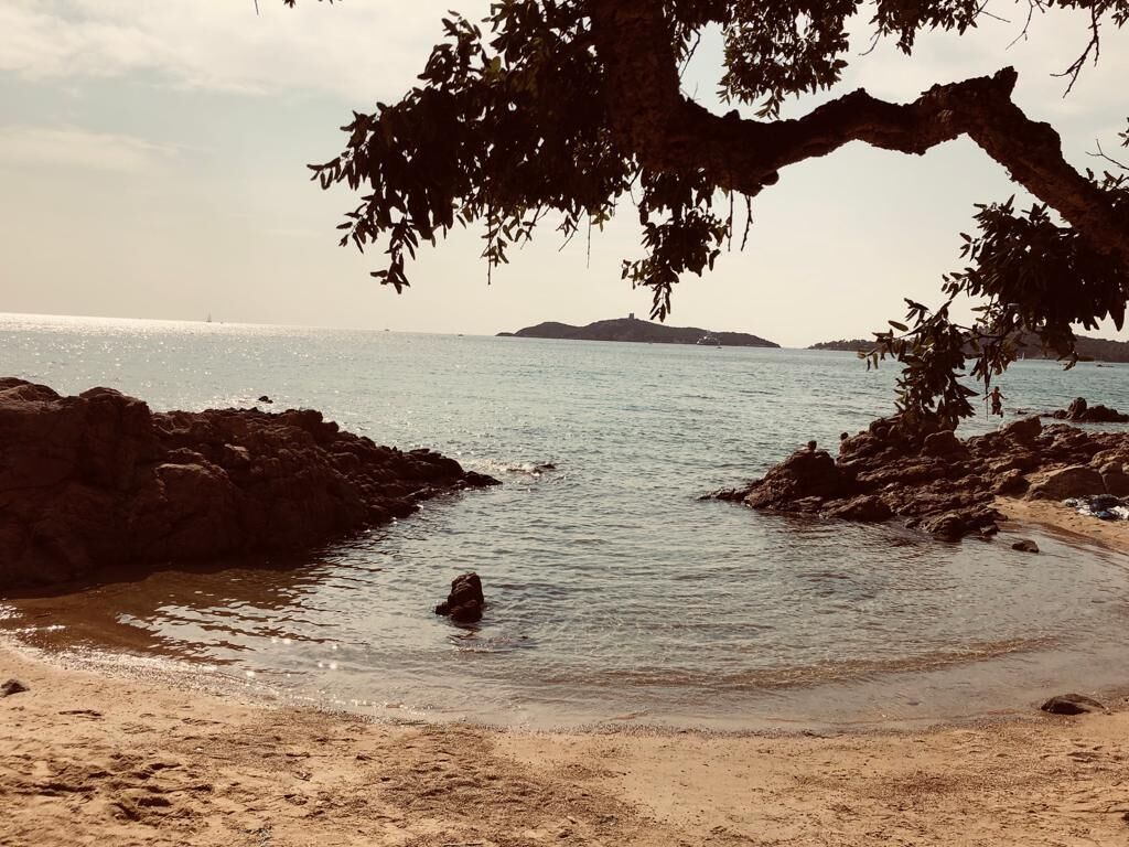 A beach with rocky shores, calm water, and a distant island.