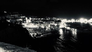 Eine Küstenstadt bei Nacht mit beleuchteten Gebäuden und Booten, die an der Uferpromenade liegen.