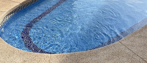 Una piscina con borde de mosaicos y un borde con textura de guijarros.