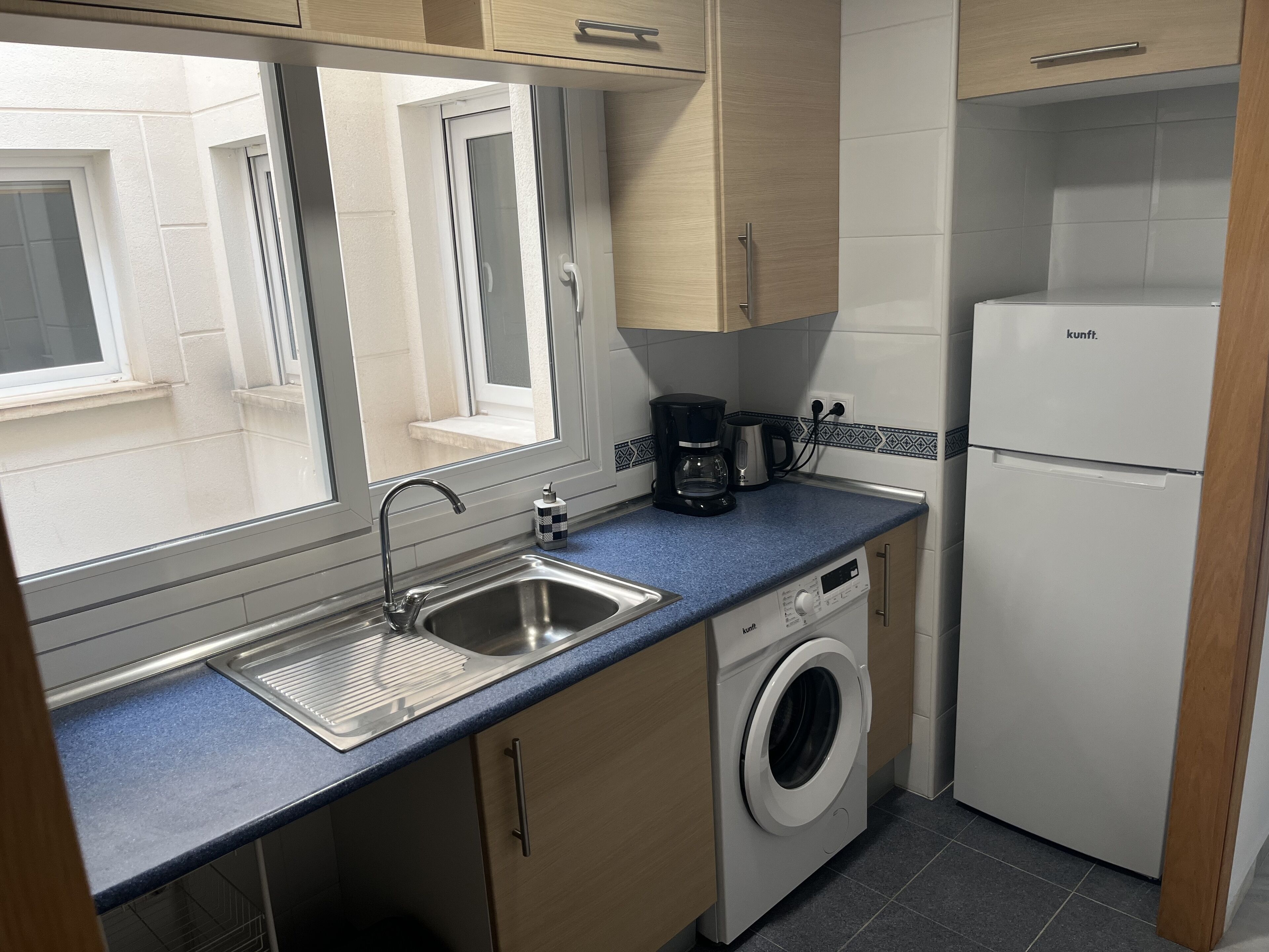 Une cuisine compacte équipée d’un lave-linge, d’une machine à café et d’un réfrigérateur.