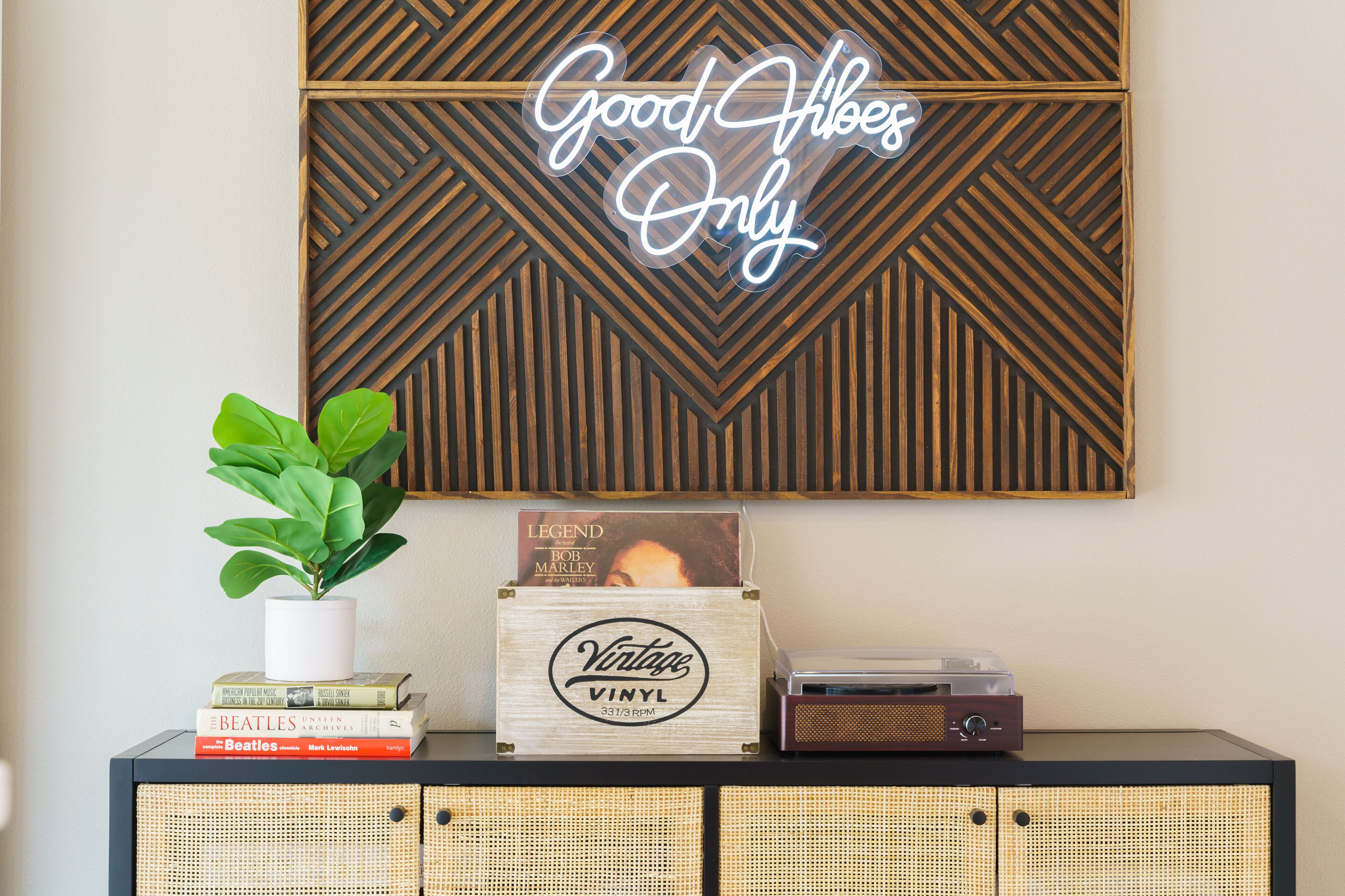 Una stanza con un neon a parete, una pianta in vaso, un giradischi in vinile vintage e una scatola di legno con l'etichetta 'Vintage Vinyl'.