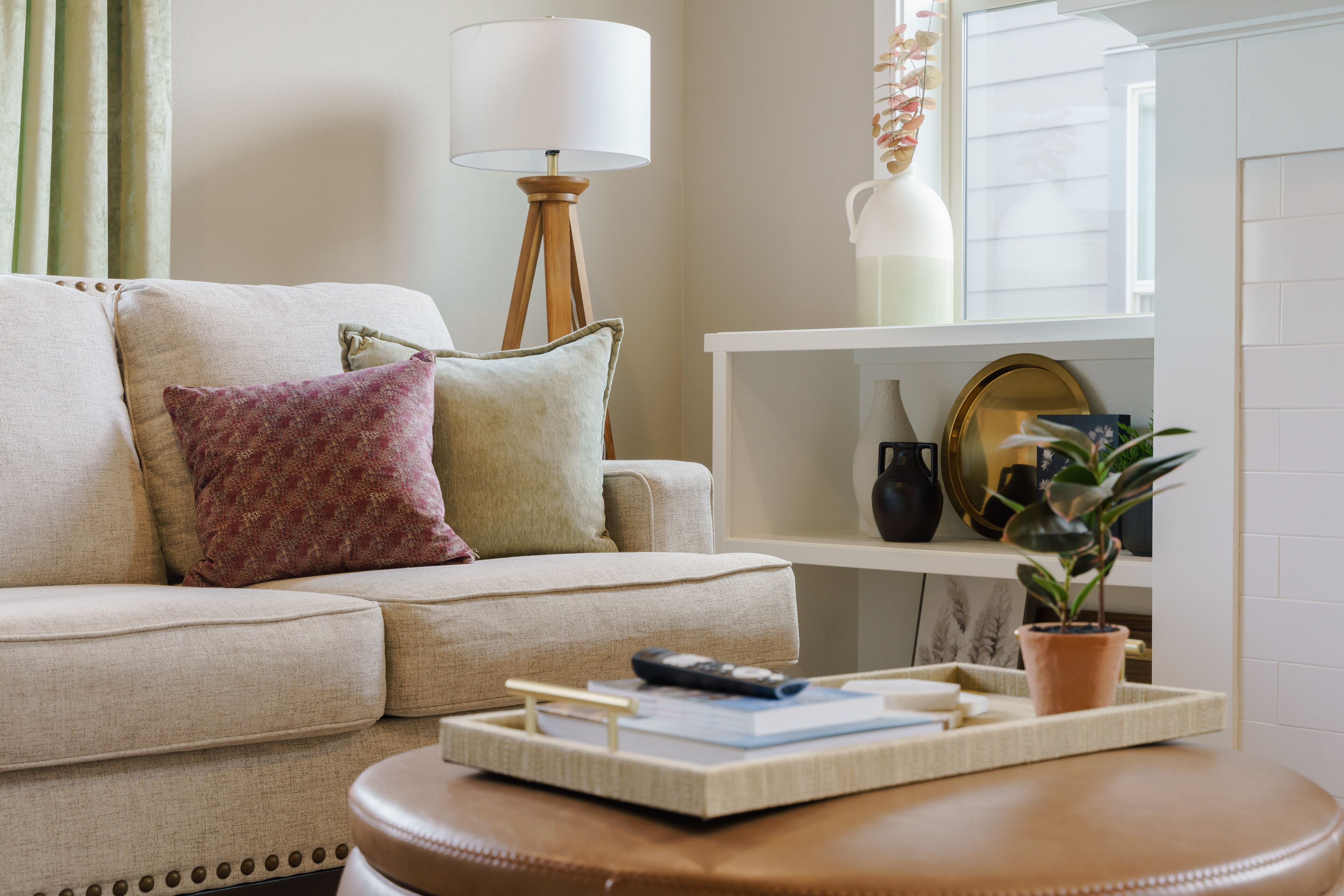 Un salon avec un canapé beige, une petite table ronde, une lampe et une étagère ornée d’objets décoratifs.