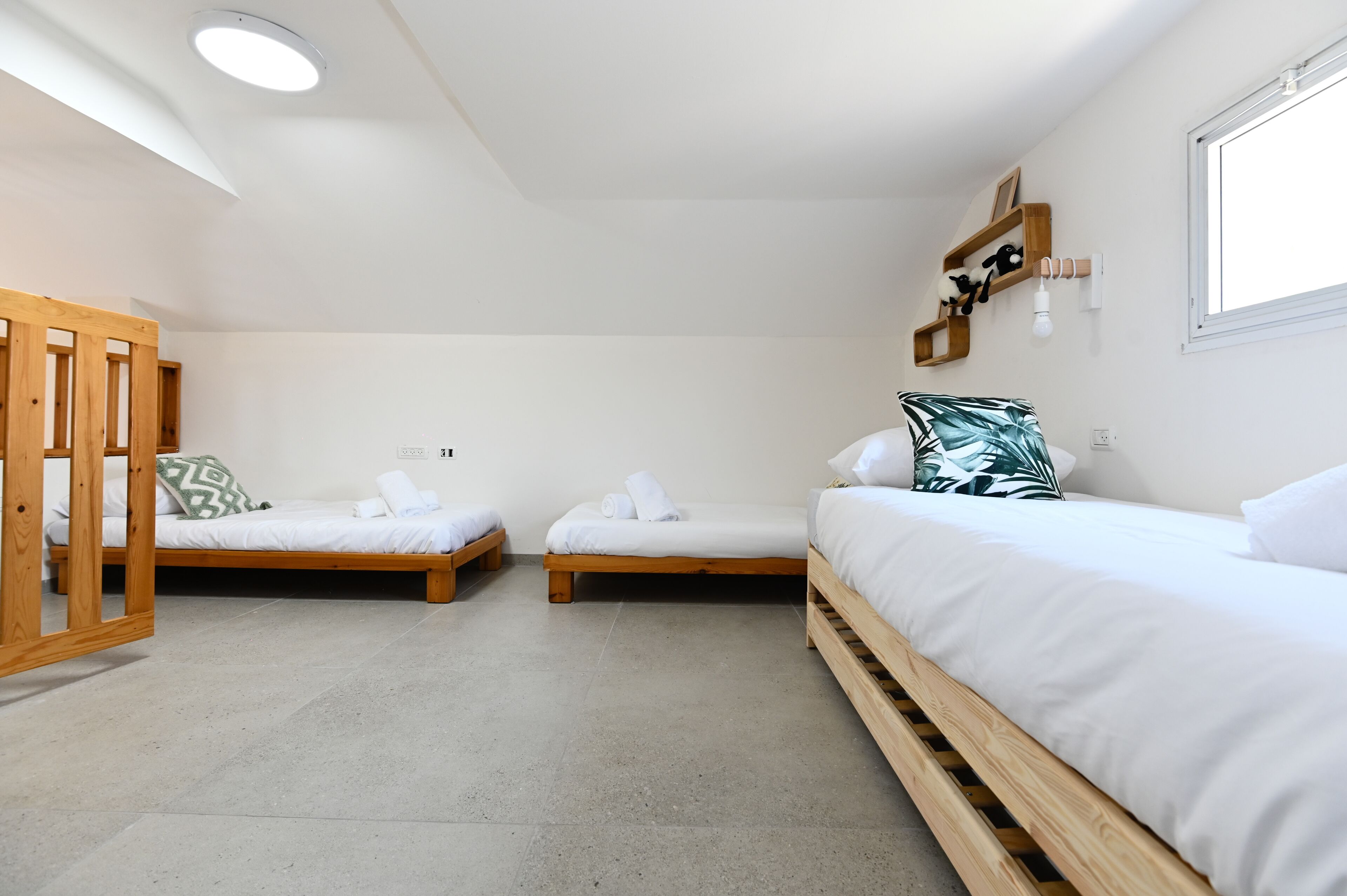 A modern, minimalist room with three wooden beds arranged in a row, white bedding, and a large window providing natural light.