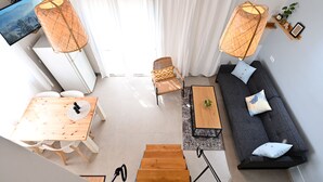 A modern living room with a wooden dining table, a sofa with patterned cushions, and a TV mounted on the wall. - YalaRent Valley view Boutique cottages (Emek Izrael)