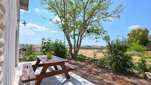 A wooden picnic table with benches, a potted plant, and a view of a tree and landscape. - YalaRent Valley view Boutique cottages (Emek Izrael)