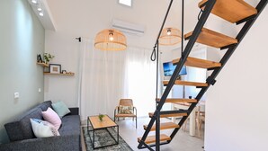 A modern living room with a grey sofa, a coffee table, a wicker chair, and a wooden staircase. - YalaRent Valley view Boutique cottages (Emek Izrael)