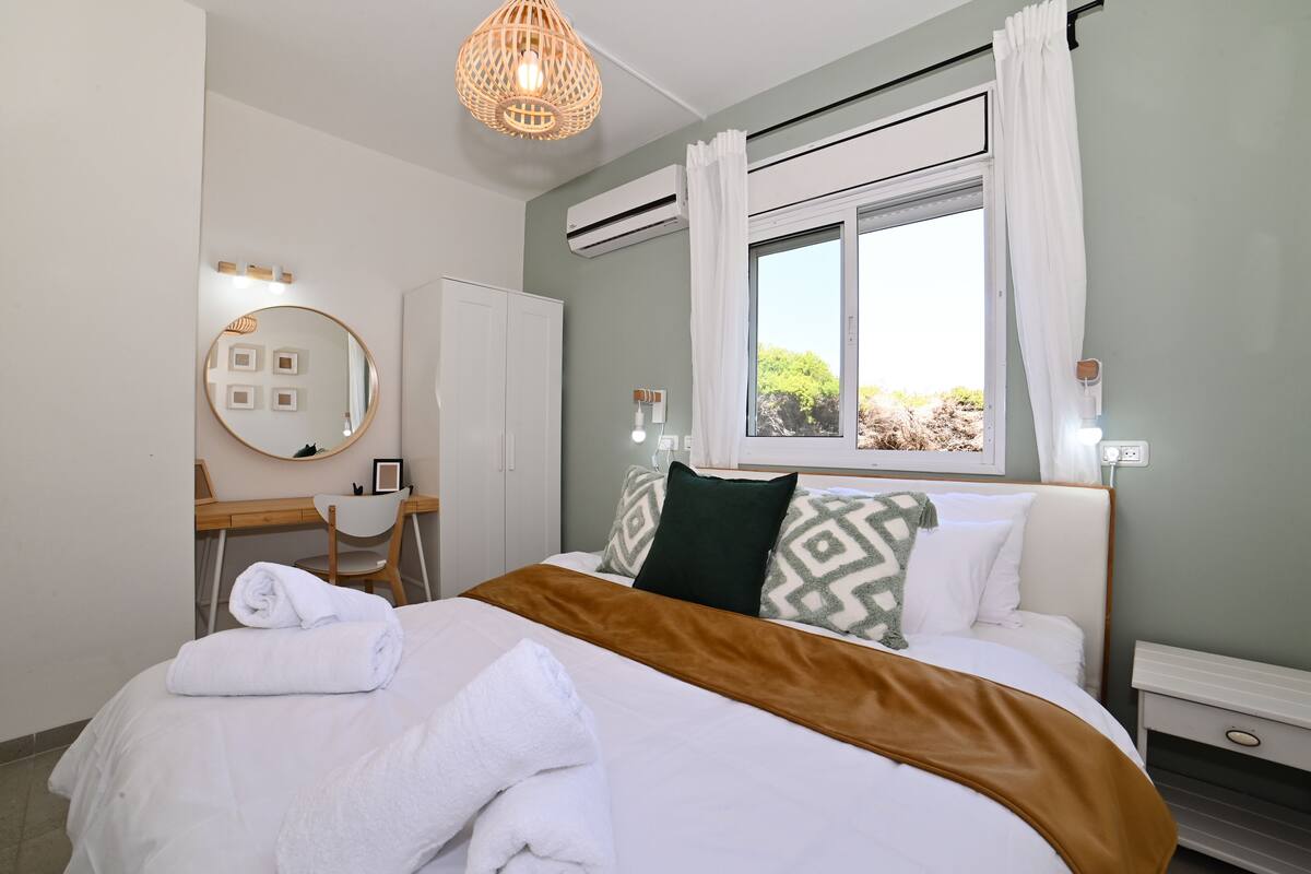 Habitación de hotel con cama, escritorio, silla, espejo y ventana con cortinas.