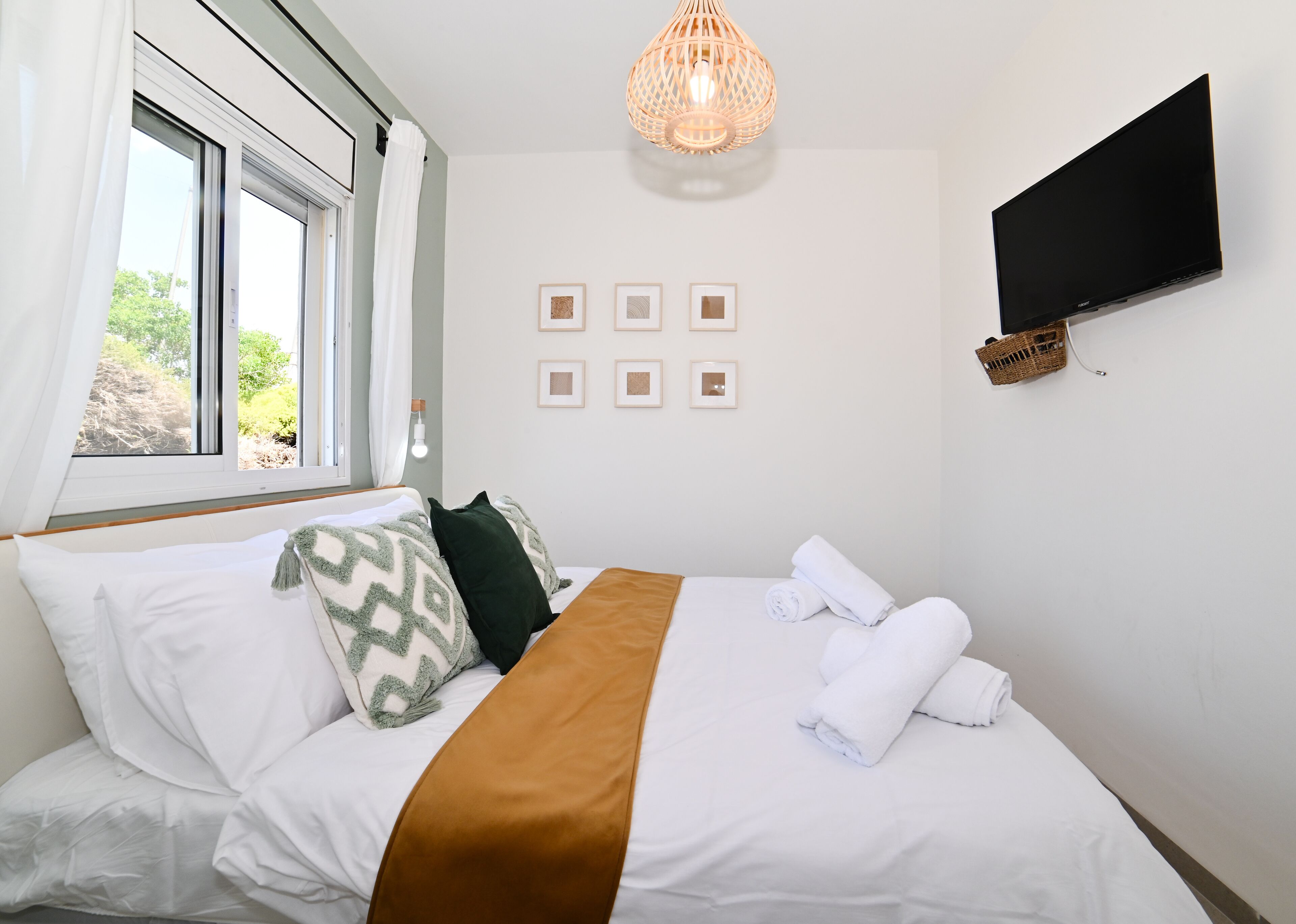 Une chambre d’hôtel avec un lit, une télévision, une fenêtre avec des rideaux et un luminaire fixé au mur.