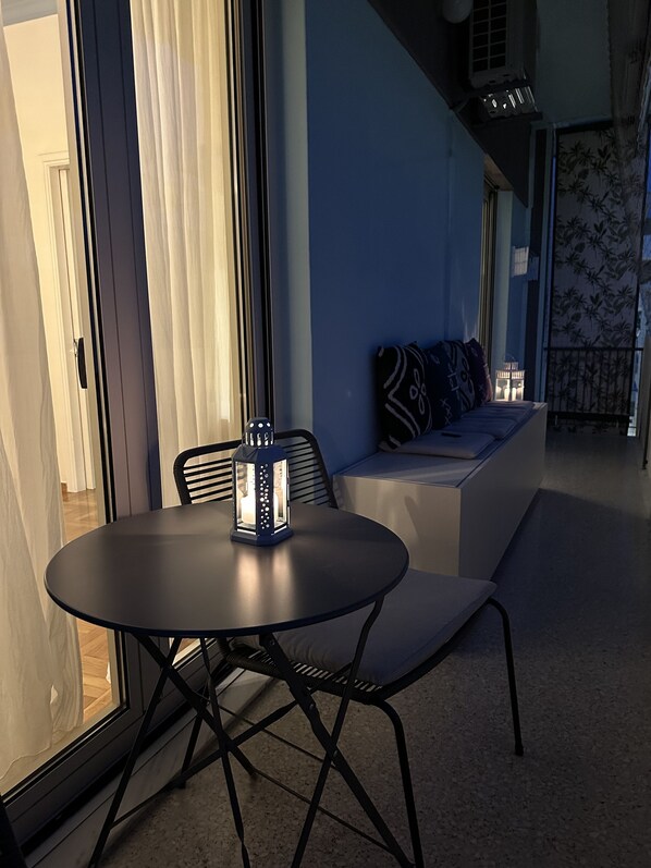 A modern living room with a round table, black chairs, a sofa with patterned cushions, and a large window with curtains.