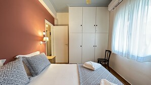 Hotellihuone, jossa on sänky, tuoli, vaatekaappi ja ikkuna, jossa on verhot.