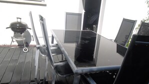 Una mesa con cubierta de vidrio, sillas de metal, una parrilla y una escalera.