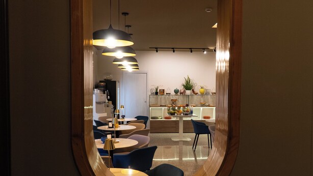 A modern dining area with round tables and blue chairs, a kitchen with a fruit bowl, and pendant lighting. - HOTEL BELVEDERE (Canicatti)
