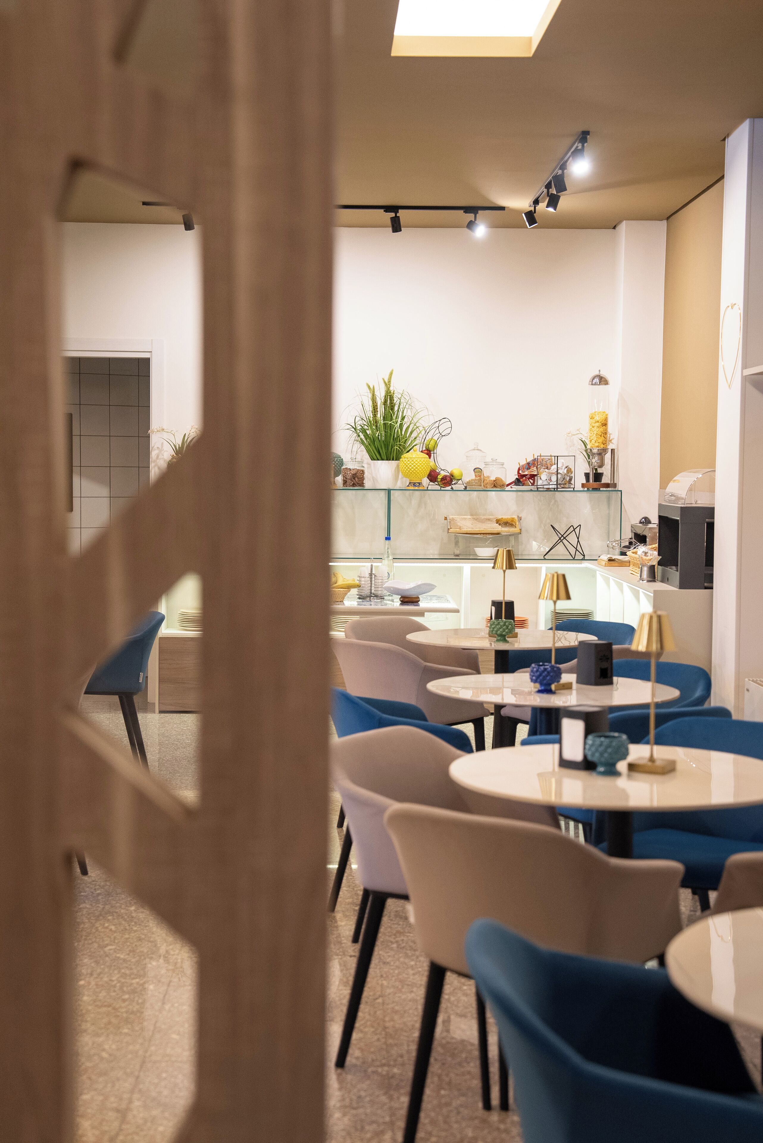Comedor moderno con mesas redondas y sillas azules, una cocina al fondo y una vista a través de una puerta.