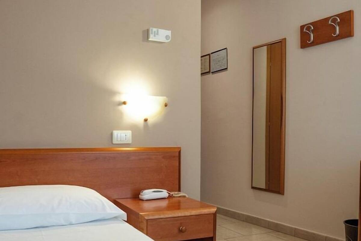 A hotel room with a bed, bedside table, lamp, and a mirror on the wall.