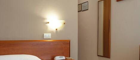 Una habitación de hotel con una cama, mesita de noche, lámpara y un espejo en la pared.