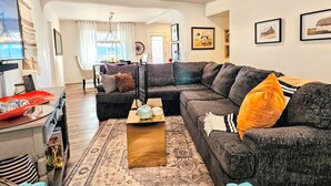Un salon moderne avec un canapé d’angle, une table basse et un coin repas à l’arrière-plan.