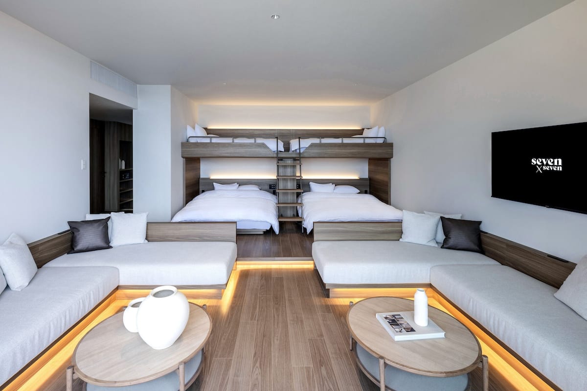 A modern hotel room with bunk beds, a sofa, a TV, and a small table with a vase.