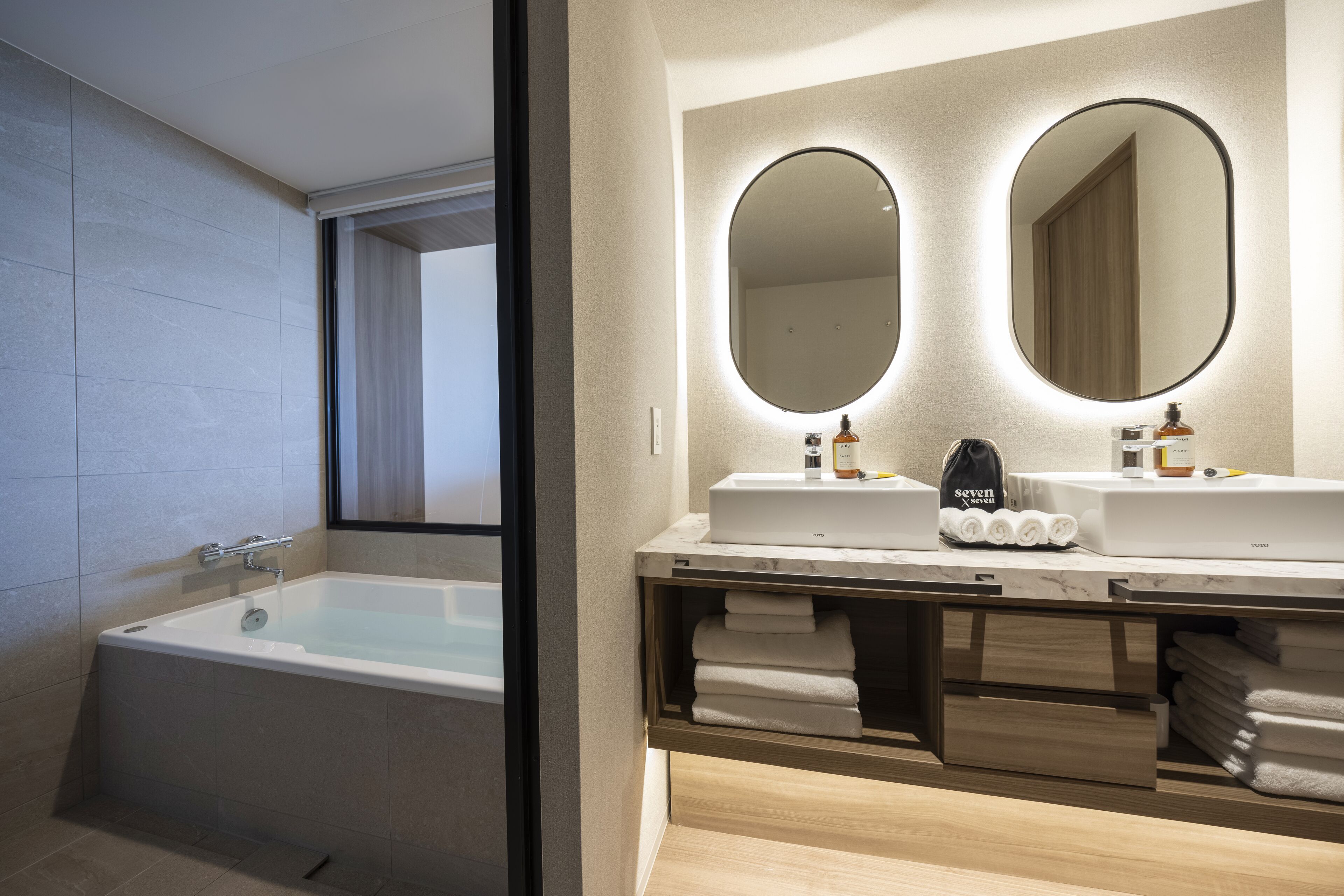 A modern bathroom with a bathtub, two sinks with mirrors, and neatly folded towels.