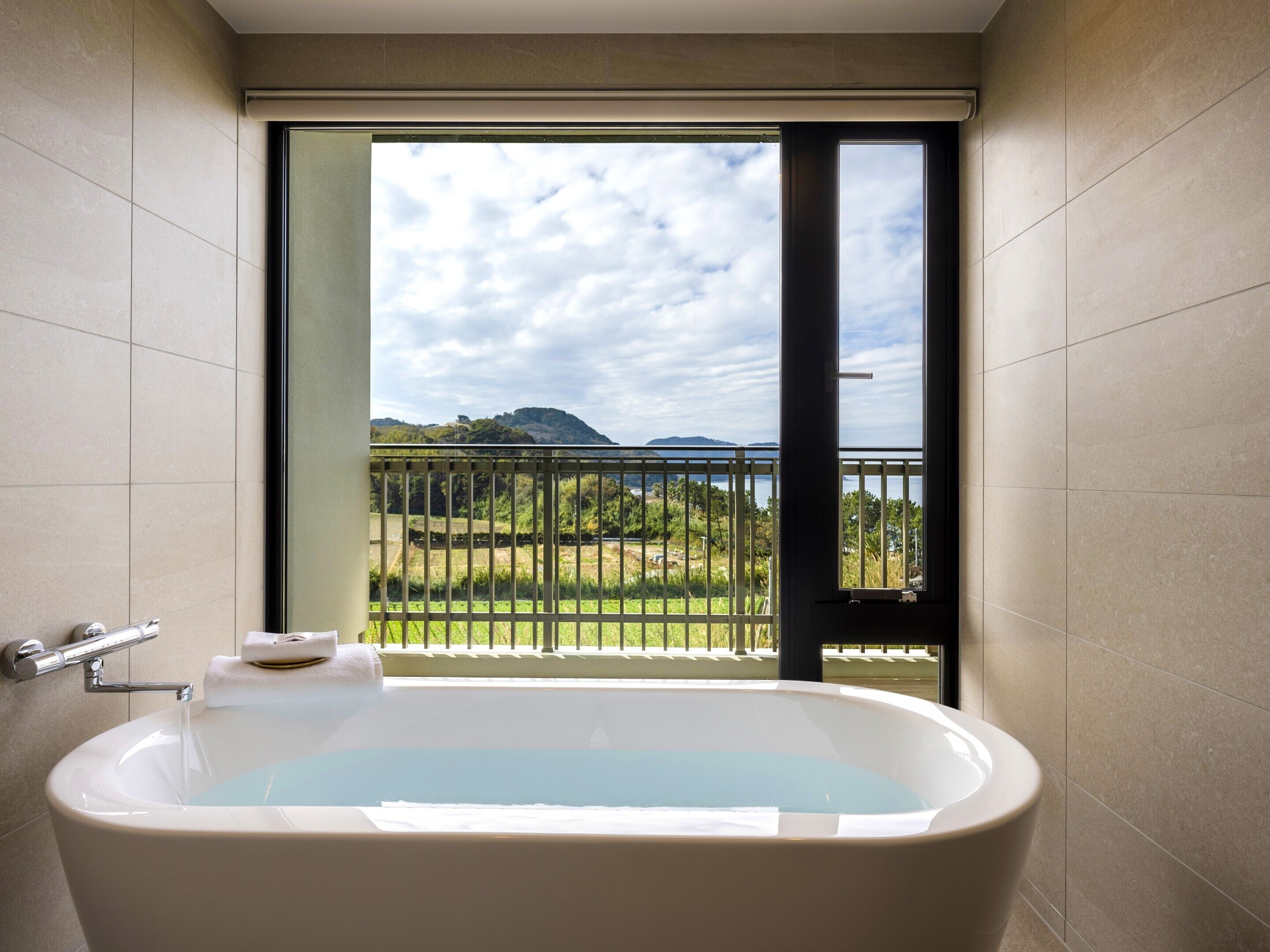 A bathroom with a bathtub, a window with a view of a landscape, and a towel rack.
