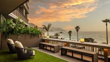 A deck with seating and a view of the ocean at sunset.