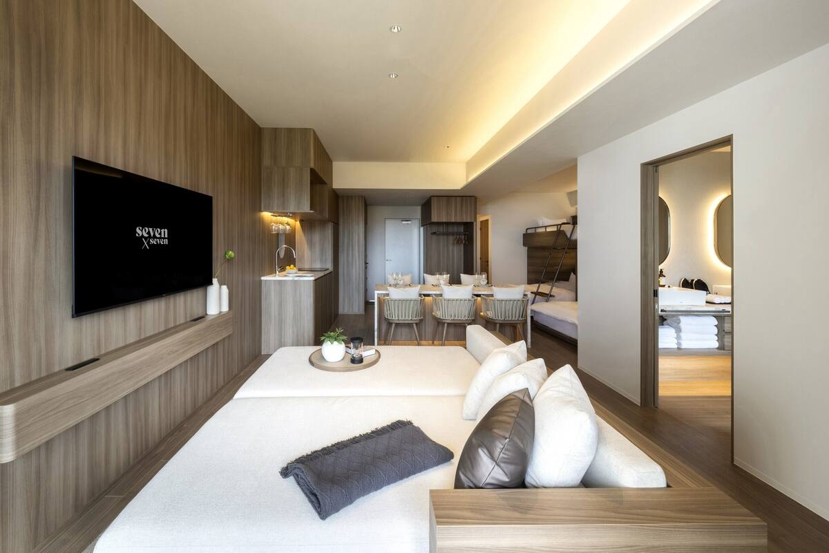 A modern hotel room with a flat-screen TV, a dining area, a kitchen, and a bathroom.