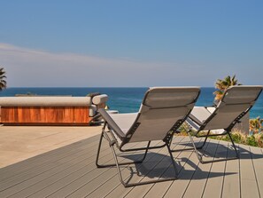 Two lounge chairs on a wooden deck with a view of the ocean.