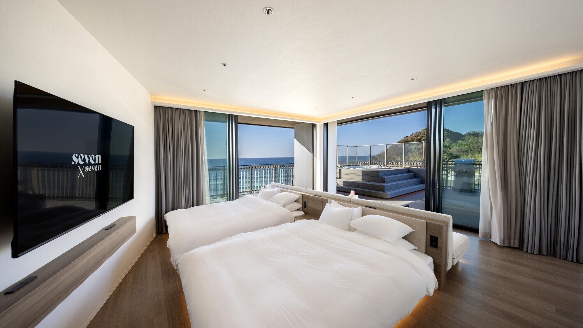 A modern hotel room with a large bed, a TV, and a balcony with a view of the sea.