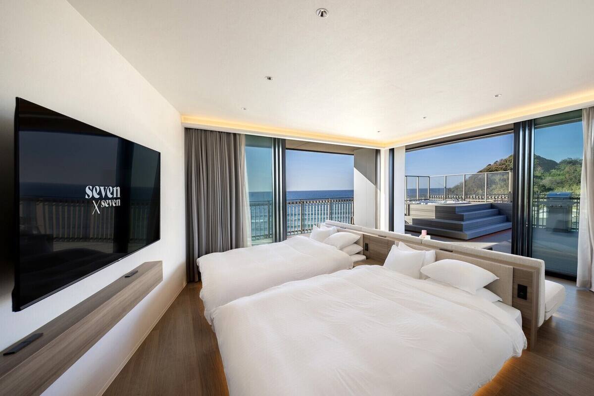 A modern hotel room with a large bed, a TV, and a balcony with a view of the sea.