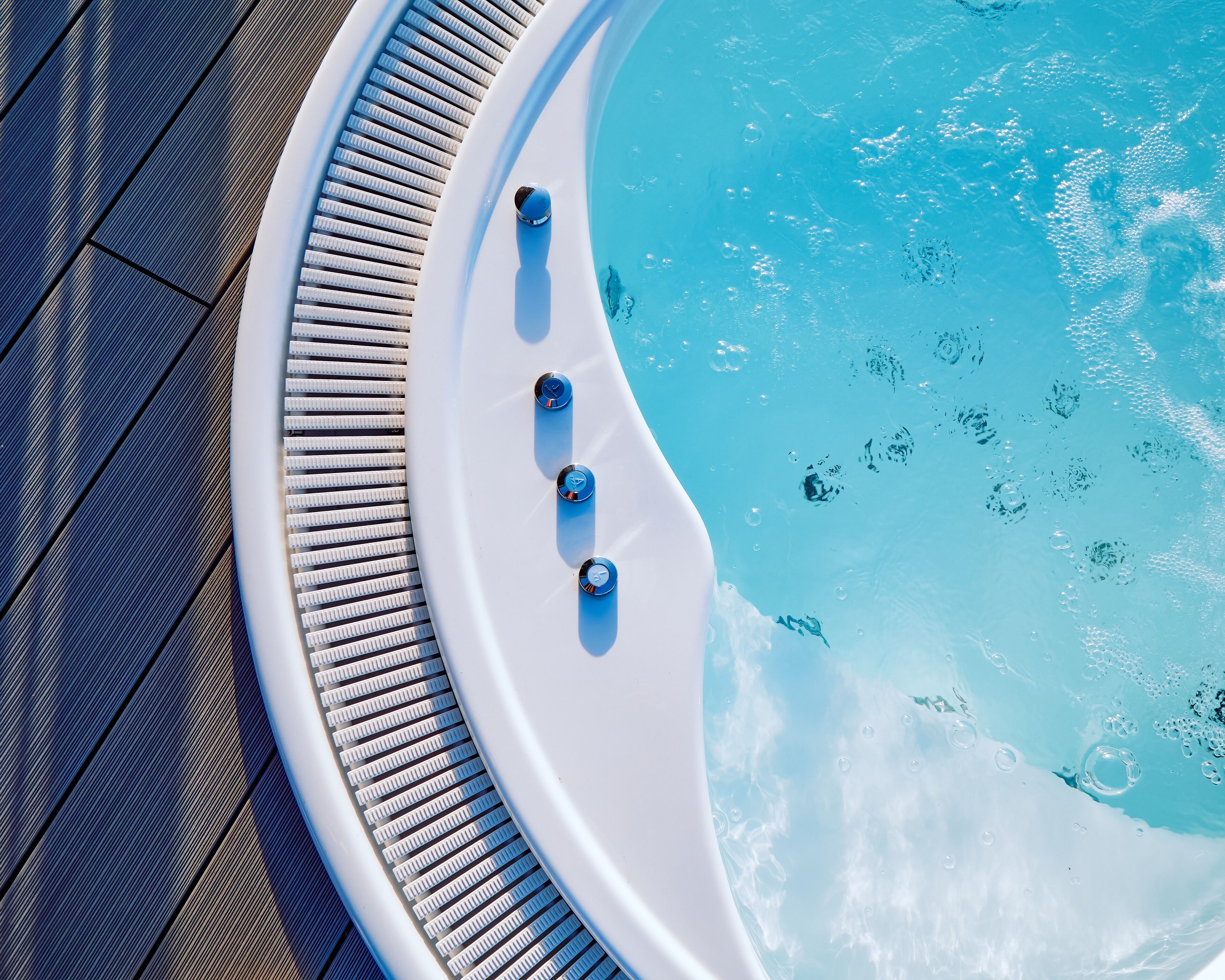 A hot tub with three controls, surrounded by a wooden deck.