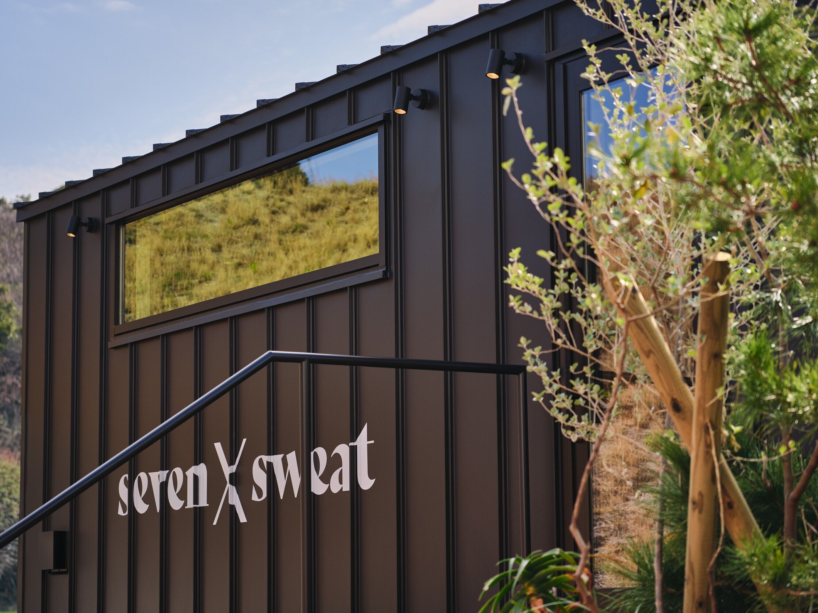 Un edificio con un letrero que dice 'sevenXswear' y una ventana que refleja un paisaje.