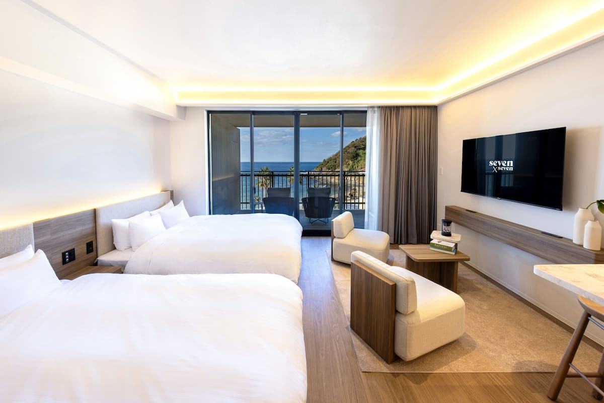 A hotel room with two beds, a TV, a balcony with a view, and a small seating area.