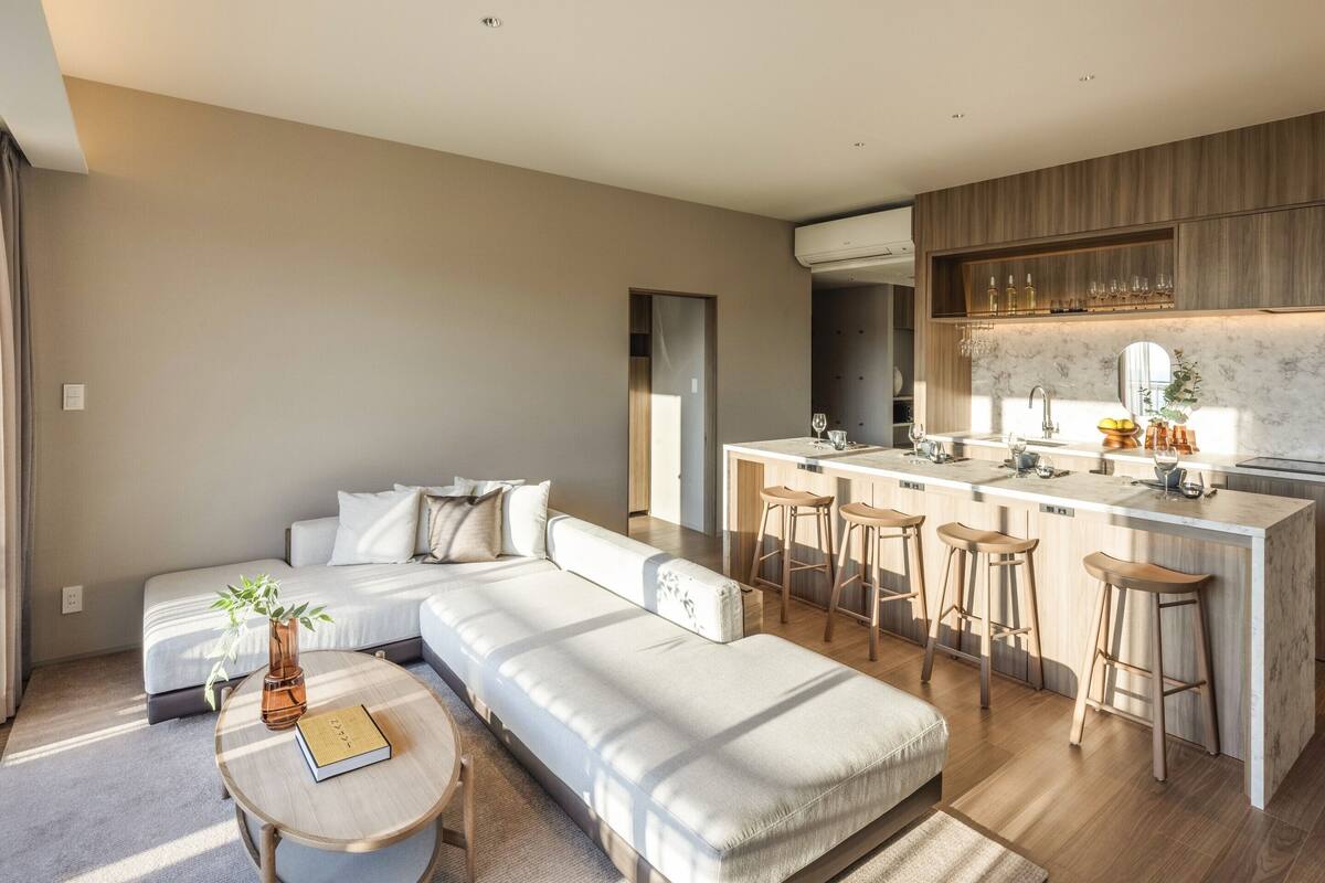 A modern living room with a large L-shaped sofa, a round coffee table, and a kitchen area with a marble countertop and bar stools.