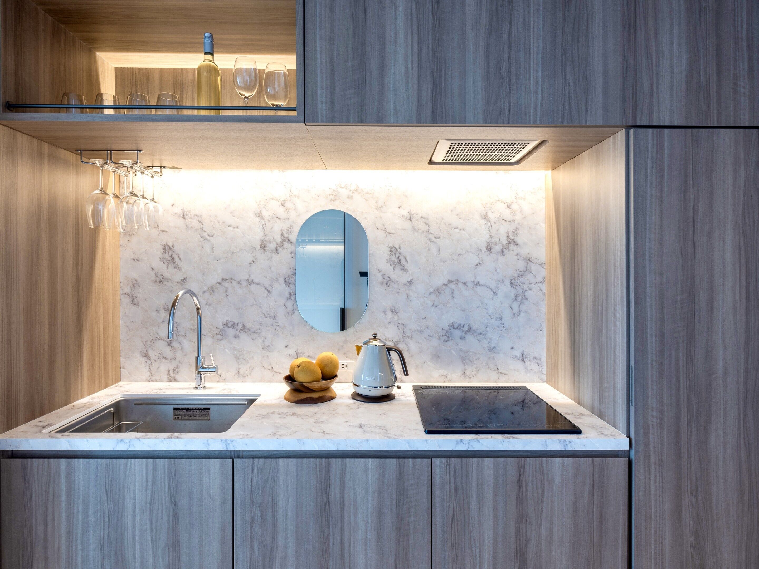 A modern kitchen with a marble countertop, a built-in sink, a stainless steel faucet, a kettle, and a wine bottle.