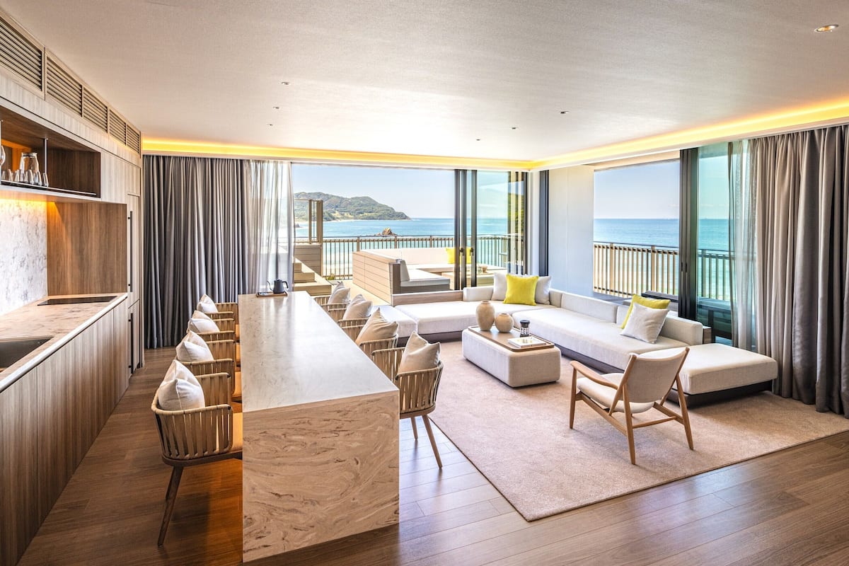 A modern hotel room with a long bar, seating area, and a view of the sea.