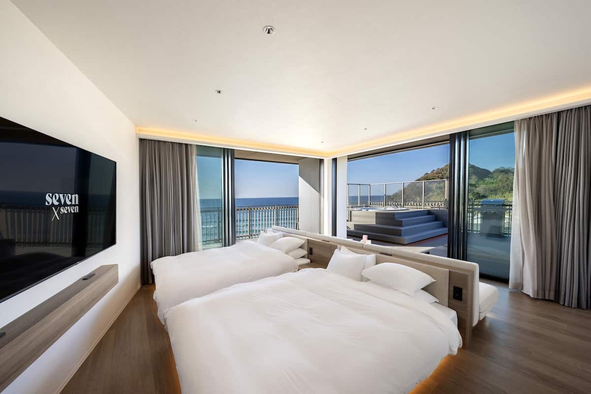 A modern hotel room with a large bed, a TV, and a balcony with a view of the sea.