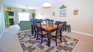 Uma área de refeições com mesa e cadeiras de madeira, tapete estampado e ventilador de teto.