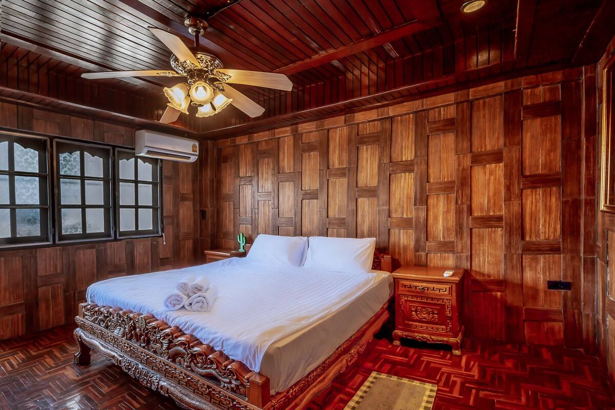 Une chambre aux murs lambrissés, avec un grand lit, un ventilateur de plafond et une fenêtre.