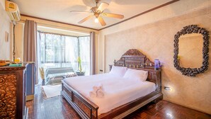 A hotel room with a large bed, a ceiling fan, a window with curtains, a wooden dresser, and a mirror on the wall. - Blue Dream Guesthouse (Chiang Mai)