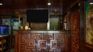 A bar area with a wooden counter, a flat-screen TV mounted above, and a decorative door with intricate carvings. - Blue Dream Guesthouse (Chiang Mai)