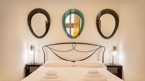 A neatly made bed with towels, a headboard with a unique design, and three wall-mounted mirrors. - Verincanto Suite In old Verona Downtown (Verona)