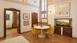 A dining area with a round table, yellow chairs, a red vase, and a painting of a street scene. - Verincanto Suite In old Verona Downtown (Verona)