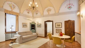 A living room with a sofa, a dining table with chairs, a chandelier, and a wooden cabinet. - Verincanto Suite In old Verona Downtown (Verona)