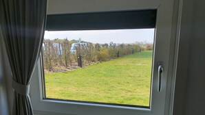 A window with a view of a grassy field and a parked car outside.